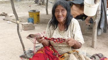 Mulher do povo Manjui sentada, trabalhando em um tecido à base de fibras vegetais