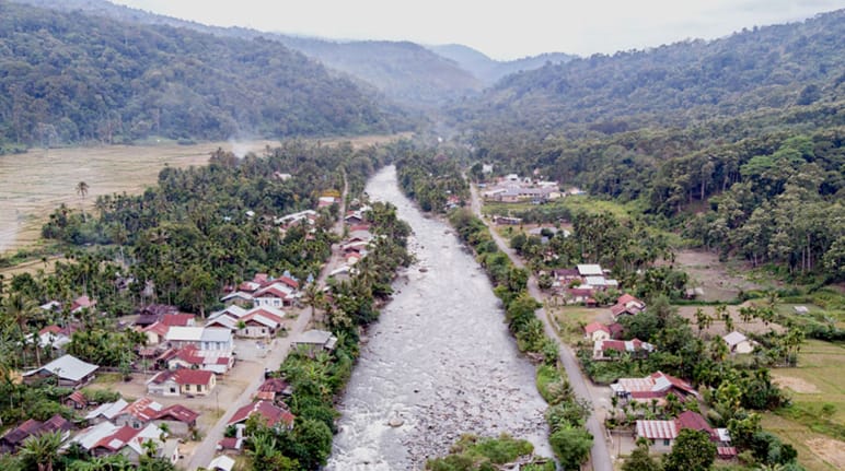 Rio passando pela aldeia com montanhas ao fundo