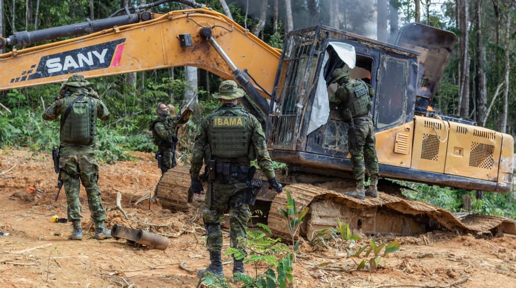 Grupo de homens vestidos com uniformes de camuflagem do IBAMA destrói escavadeira na floresta amazônica