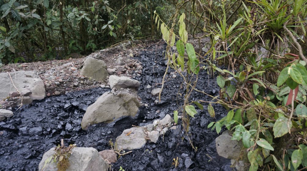 Fluxo de petróleo bruto derramado sobre uma área coberta de cascalho e pedras