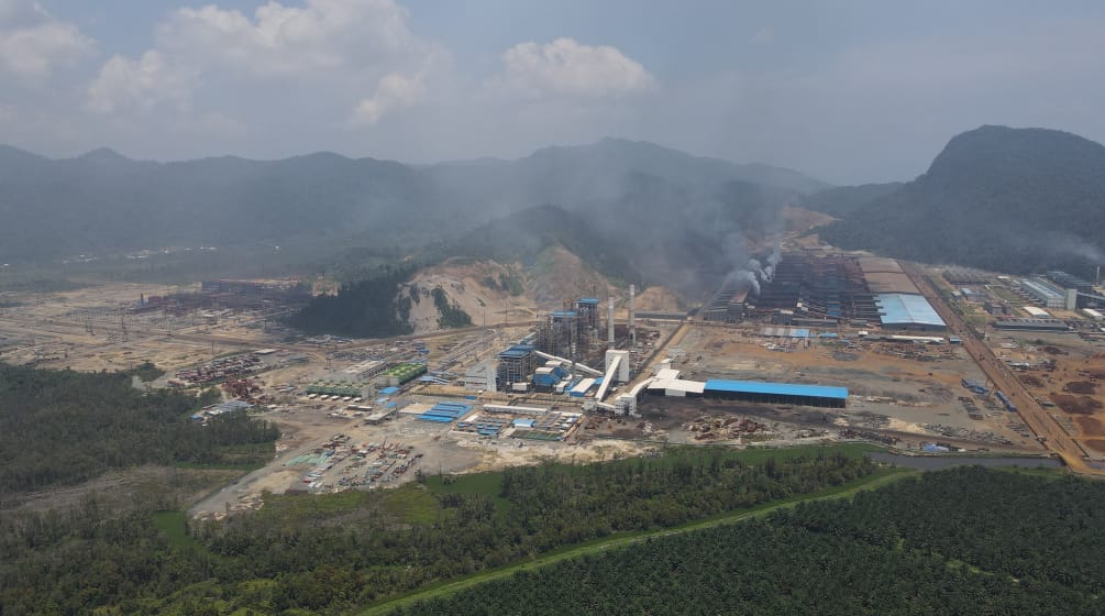 Vista aérea de um complexo industrial soltando fumaça na ex-floresta tropical, agora devastada.