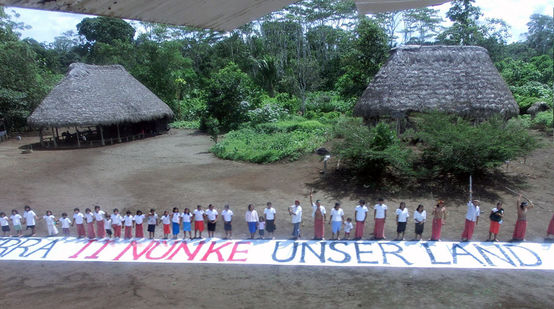 Os indígenas em uma aldeia na selva amazônica dirigam-se ao público com uma bandeira: Isto é nossa terra.