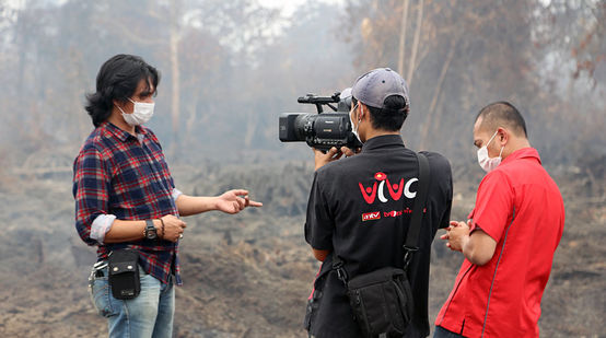 Um homem está sendo entrevistado à frente de uma floresta tropical em chamas