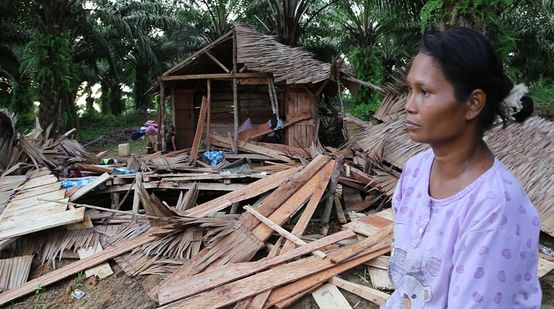 Uma indígena está sentada perturbadamente diante as ruínas da sua casa